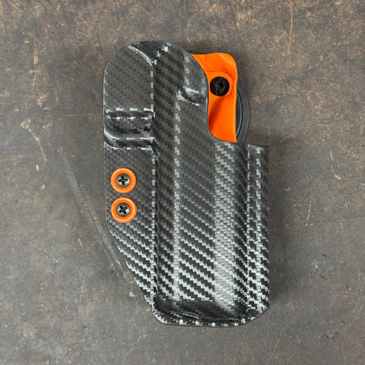 Carbon fiber patterned holster with orange accents on a dark surface