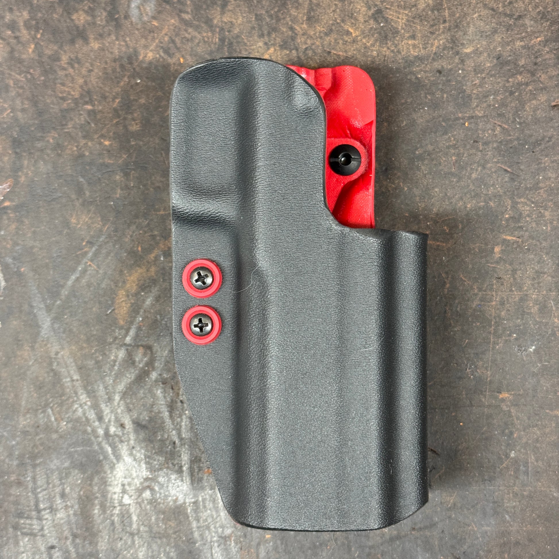 Black gun holster with red fastening screws on a textured surface